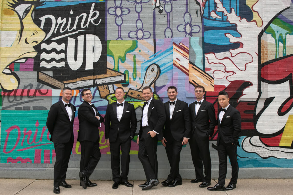 Groom poses with friends in front of graffiti wall