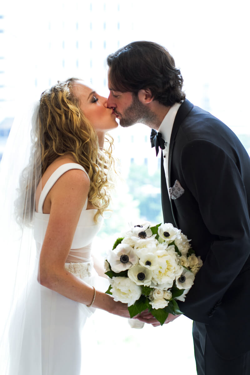Bride and groom kissing in window light